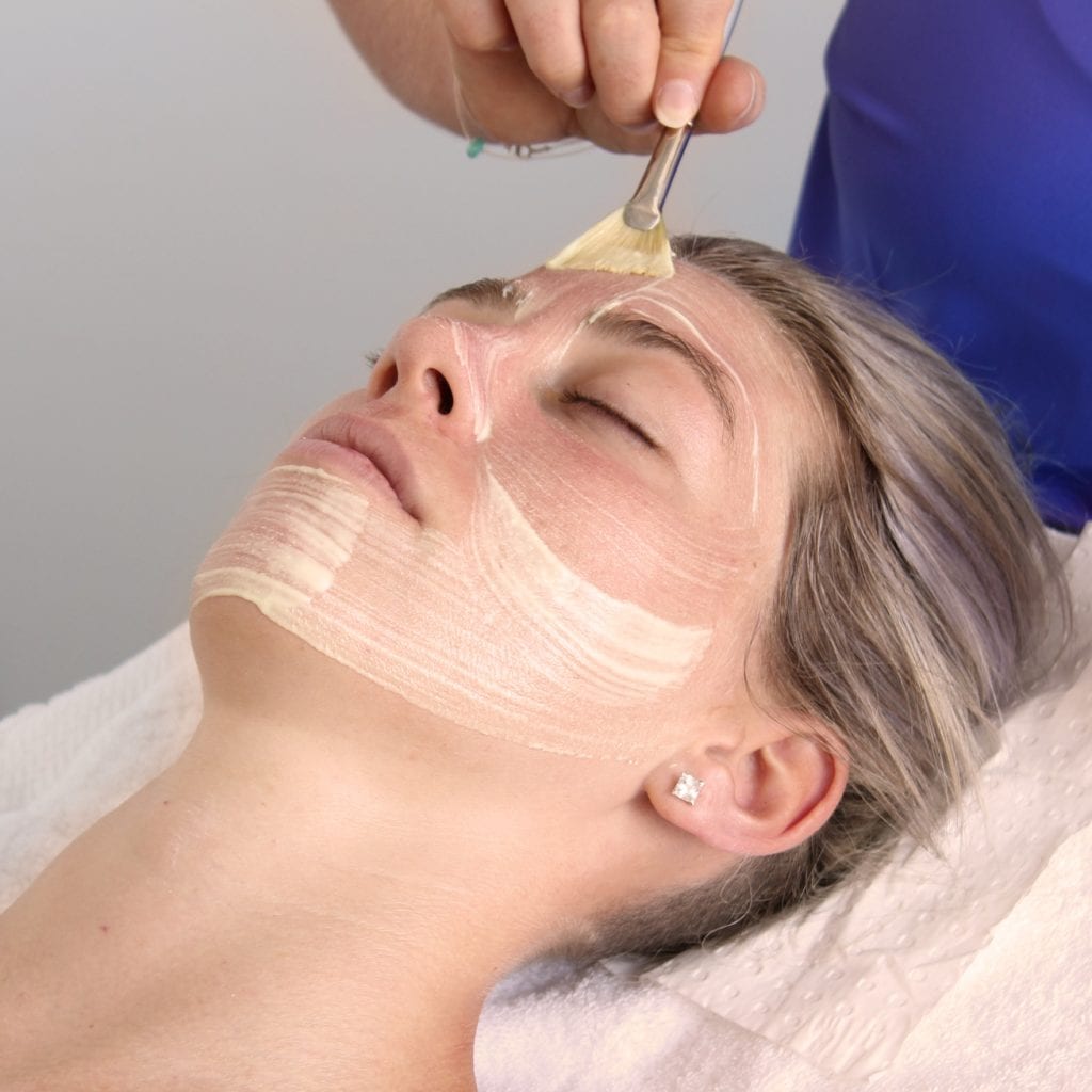 Young woman having an O Cosmedics Dermal Planning chemical peel brushed on to her face.