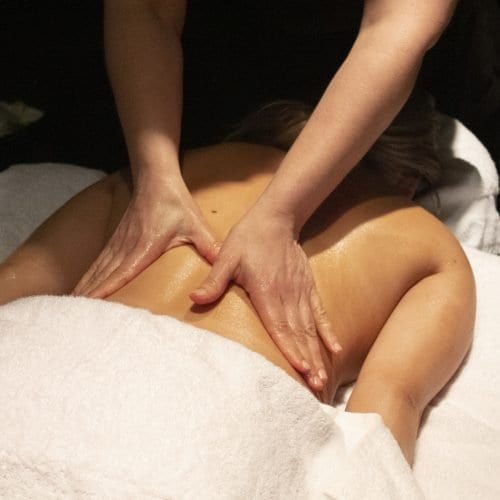 Image of Woman lying face down on a salon bed while a therapist massages her back.