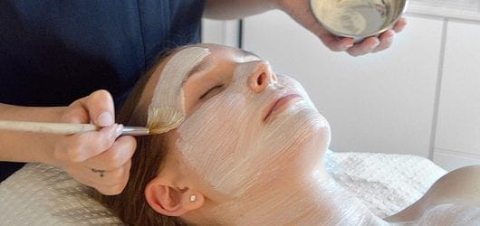 Ginger&Me Mindfulness Facial Young woman having a mask brushed on to her face.