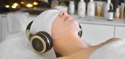 Ginger&Me Mindfullness Facial Young woman on a beauty spa bed with a towel and headphones over her head, enjoying a paper mask facial.