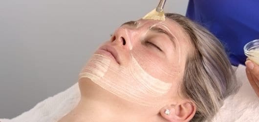 O Cosmedics Dermal Planning Peel Young woman on a beauty spa bed, having a chemical peel brushed on to her skin by a therapist.