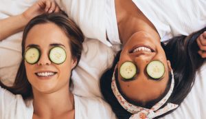 two girls lying on bed with cucumber on eyes